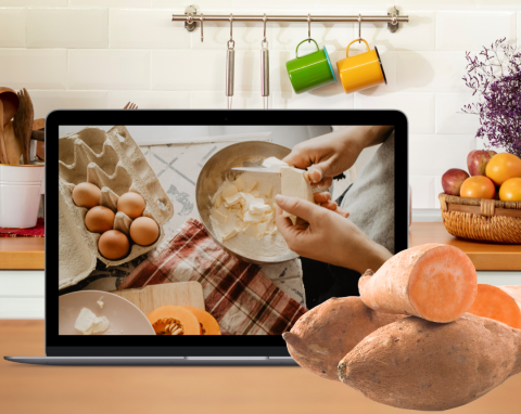 A laptop displaying someone cooking on a kitchen counter next to some sweet potatoes