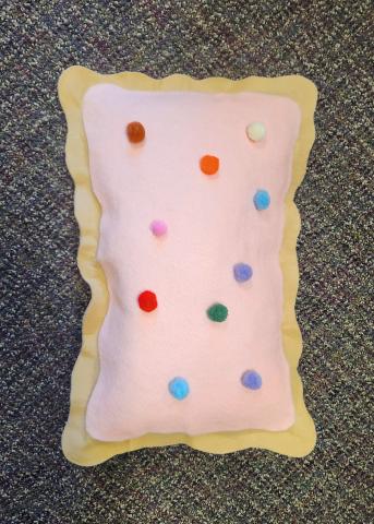 A sample image of the craft, a plush pop tart shaped pillow with light pink icing and pom pom sprinkles