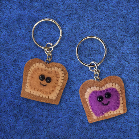 Sample of the craft being made, two small felt pieces of bread, one with a peanut butter colored blob and the other with a grape jelly colored blob. Both have tiny smiling faces sewn on.