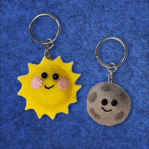 Sample of the craft being made, a small felt sun and moon. Both are attached to keychains and both have sewn on smiling faces.