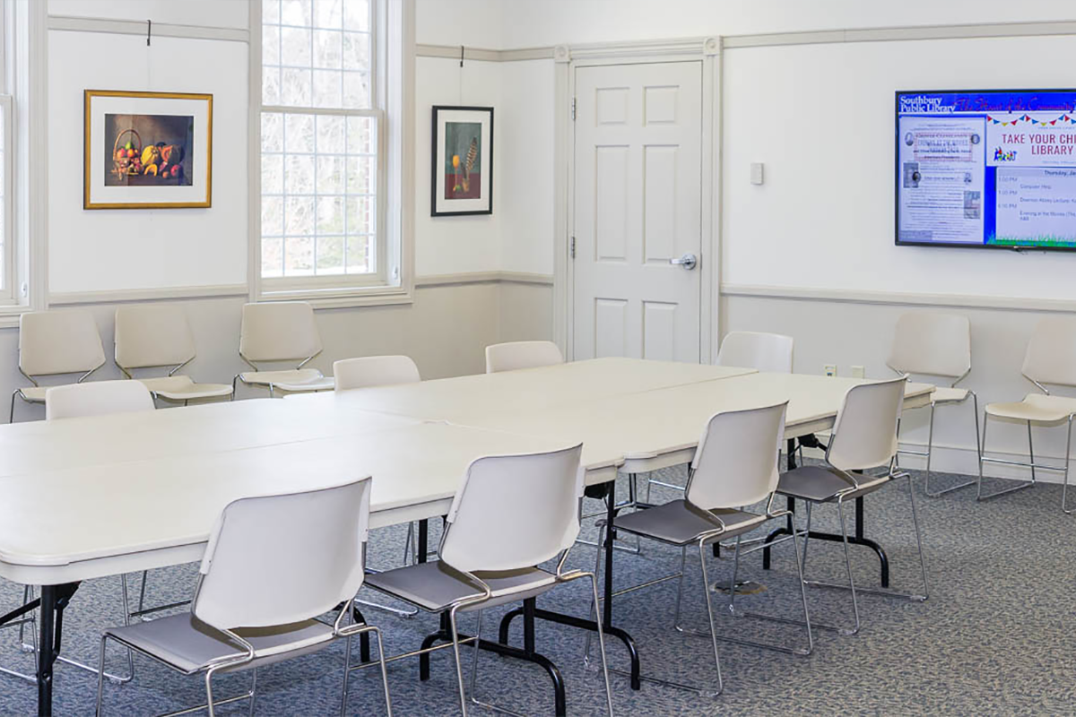 A room with one large table and chairs and a digital screen