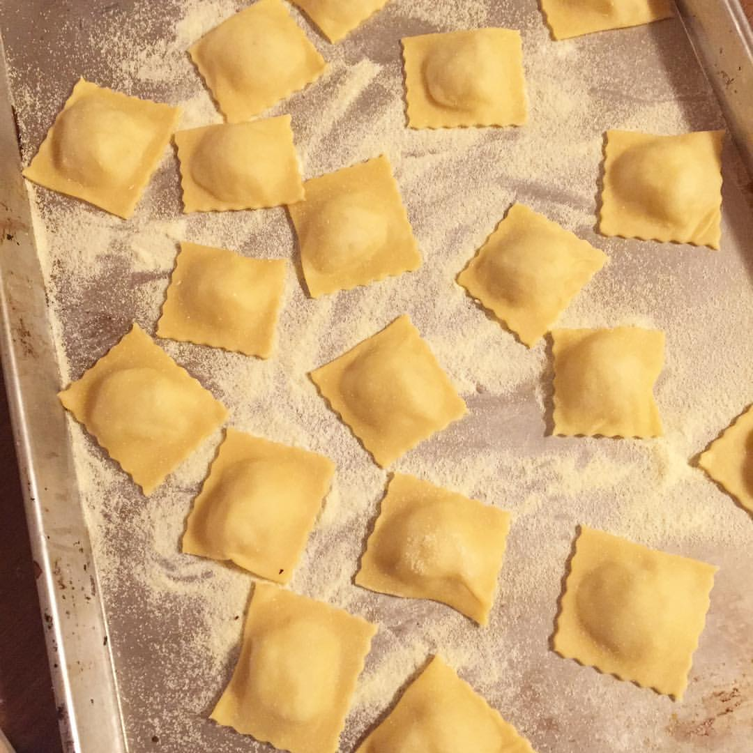 Homemade ravioli on a floured baking pan, waiting to be boiled.