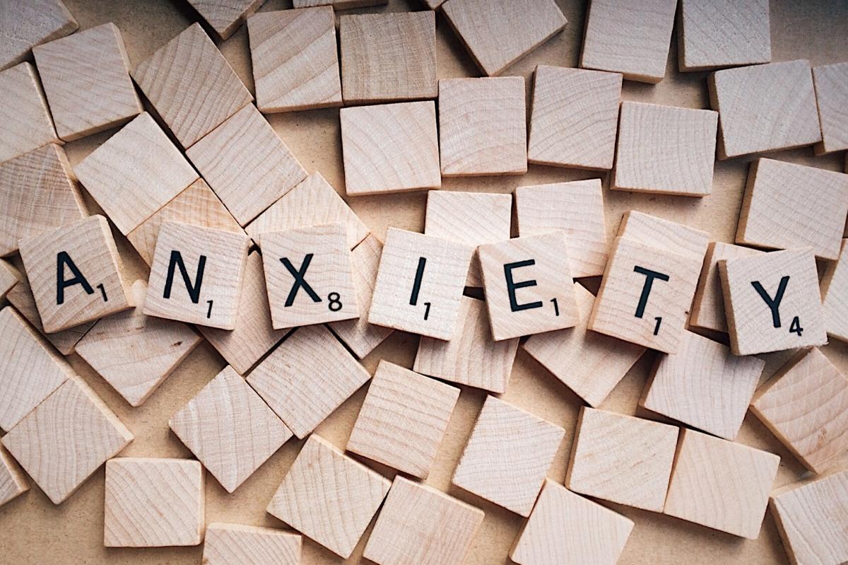 The word "anxiety" is spelled with scrabble tiles over a background of overturned scrabble tiles.