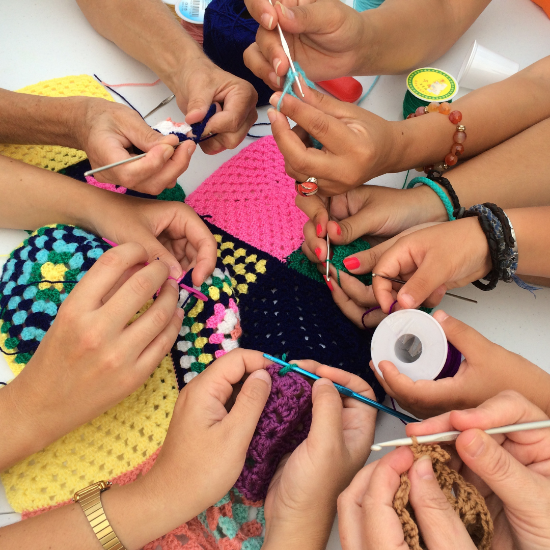 Assorted hands of varying tan shades crocheting together