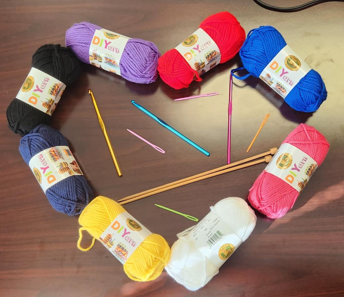 Yarn, crochet hooks, and knitting needles arranged in a heart shape on a dark wood table