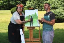 A picture of the author and artist together in front of a grass yard. They are both looking off to the distance in the right.